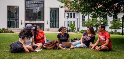 Five students sitting on the grass in front of Susan A. Cole Hall.