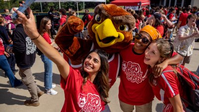A group of students wrangles Rocky the Red Hawk for a selfie at the Red Hawk Day street fair