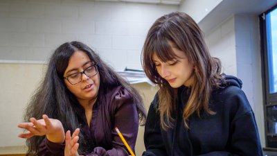 A teacher and a student are talking while the student is writing something down.