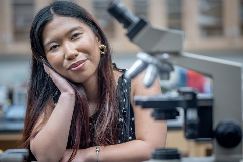 Woman is staring into the camera with her head tilted and a microscope is to her right.