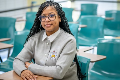 Woman is sitting down in an empty classroom smiling. 