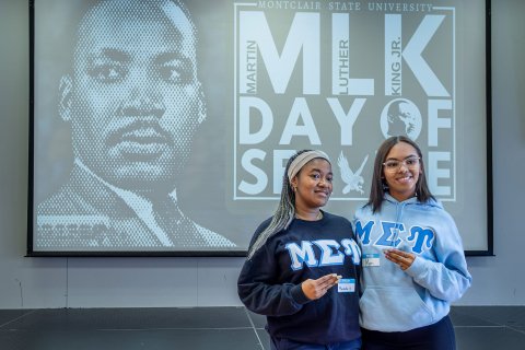 Two sorority members stand before a Martin Luther King Jr.’s Day of Service screen.