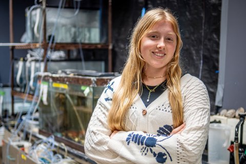 A woman in a knit sweater with lobsters on it standing in a lab full of fishtanks