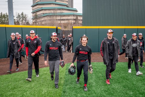 Men in black-and-red Montclair baseball uniforms walk onto a field.