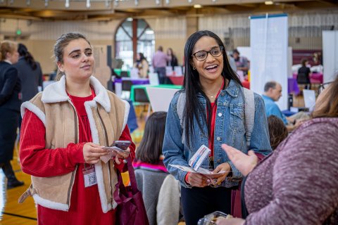 Two students smile and listen to someone speaking.