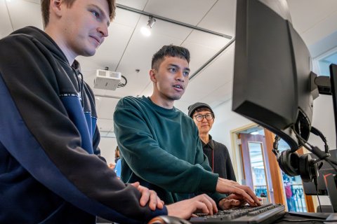 Three men are pictured looking at a computer screen intensely. 