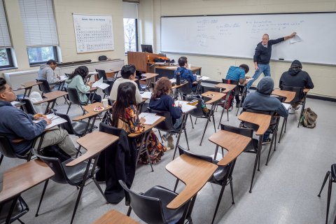 Professor teaching in front of a whiteboard to a classroom full of students. 