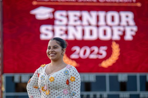 Angela Castro stands in front of a large red sign with white lettering that says Senior Sendoff 2025.
