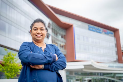 Woman in front of a hospital with her arms crossed, smiling. 