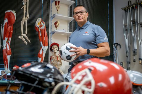 Luis Torres holds a soccer ball in a classroom filled with sports equipment.