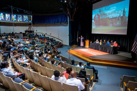 An orientation is taking place in an auditorium with a projector and stage.