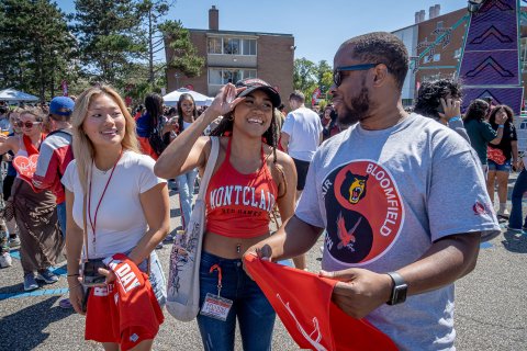 Two Montclair State University students and one Bloomfield College student stand together, chatting at an outdoor carnival.