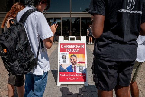 Students look at their phones in front of a sign advertising a career fair that has a QR code on it.