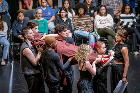 Five actors carry an actor wrapped in cloth as the audience during a performance of Richard III.