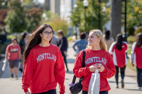 Two students in red sweatshirts walk on campus.
