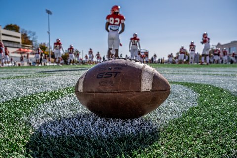 Football on the field. Football players are in the background getting ready for practice.