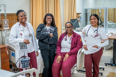 Four women smiling at the camera with their scrubs and nursing gear on. 