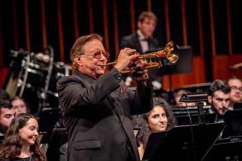 Arturo Sandoval plays the trumpet with students in the University Wind Symphony seated behind him.