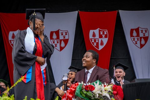 Man in cap and gown on stage proposing to woman in cap and gown