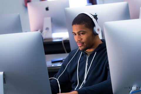 Student wearing headphones while using large-screen computer in computer lab