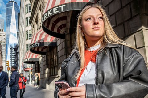 Emma Haskell stands on a sidewalk in lower Manhattan holding her phone.