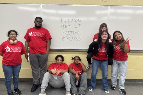 Seven student are pictured posing for the camera, three are standing, two are sitting, one is piggybacking on another. 