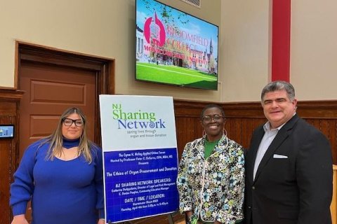 Three people are standing in front of a poster. 