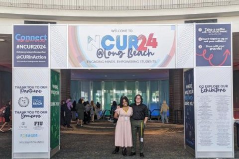 Two students are under the posters for the NCUR 2024.