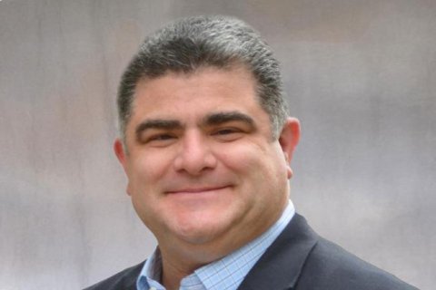 Man is smiling with a black suit on and blue dress shirt.