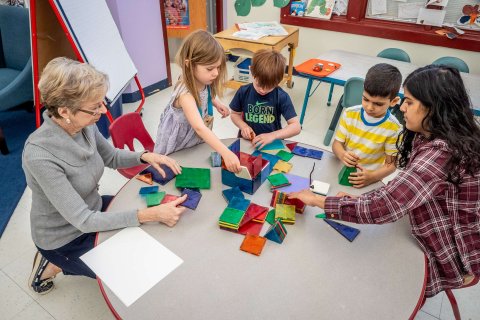 Teachers working with very young students at a low table on a class project involving colorful magnetic blocks.