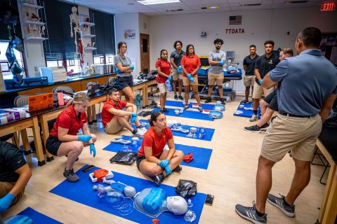 Students in a classroom with mats laid out on the floor and an assortment of training equipment arrayed on each mat.