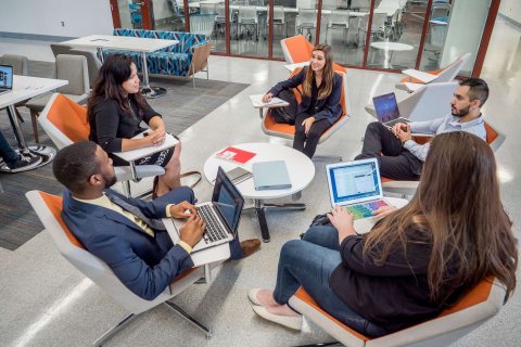 Five students in conversation, sitting in lounge chairs arranged in a circle.