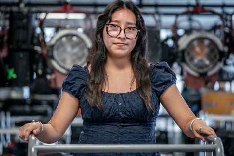 Pamela Hernandez stands in a campus broadcast media lab, surrounded by professional studio lights and equipment.