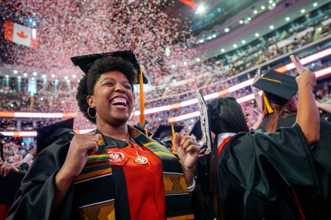Graduate in cap and gown cheering as red and white confetti fills the air during Montclair State University’s 2026 Spring Commencement at Prudential Center.