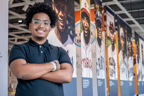 Edward Gonzalez stands with his arms crossed in front of famous ballplayers of the Negro Leagues.