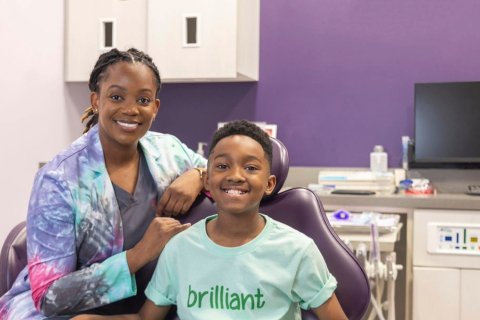 Pediatric patient sitting in dentist chair with Dr. Suffiyah Webb posing next to him 