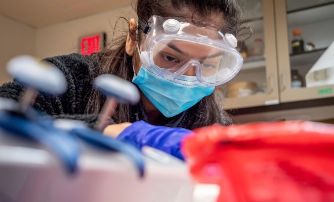Close up view of student wearing safety goggles, mask and gloves handling samples in a lab