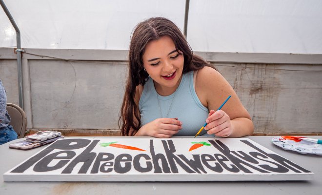 Student paints a garden sign with the Munsee language word for "carrot."