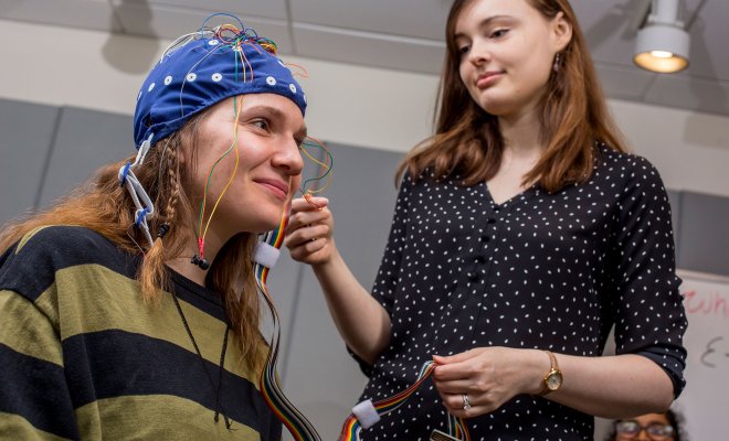 Two people studying Linguistics with a device on one of their heads.