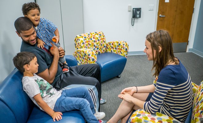 An adult sitting on couch with two children, across from another adult