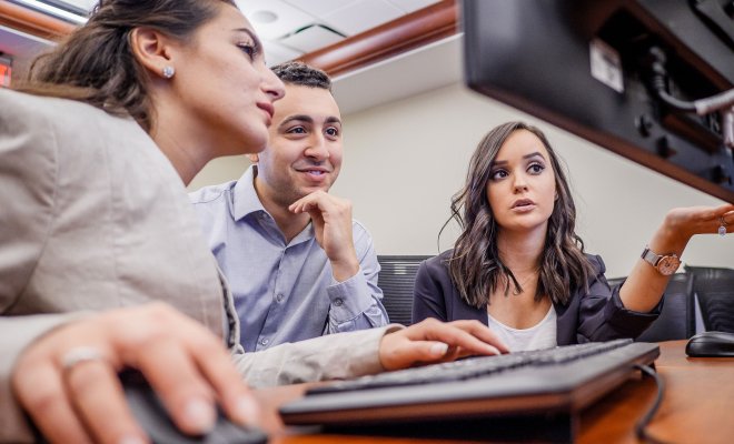three students talking in front of computer monitor