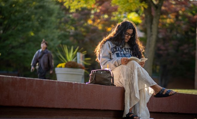 Student reading a book, sitting on a ledge on Montclair campus