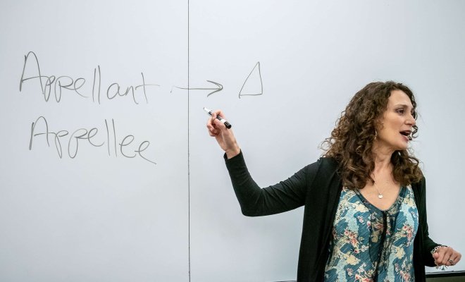 Professor Jessica Henry stands before a white board, speaking to class.