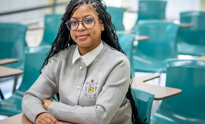 Woman is sitting down in an empty classroom smiling. 