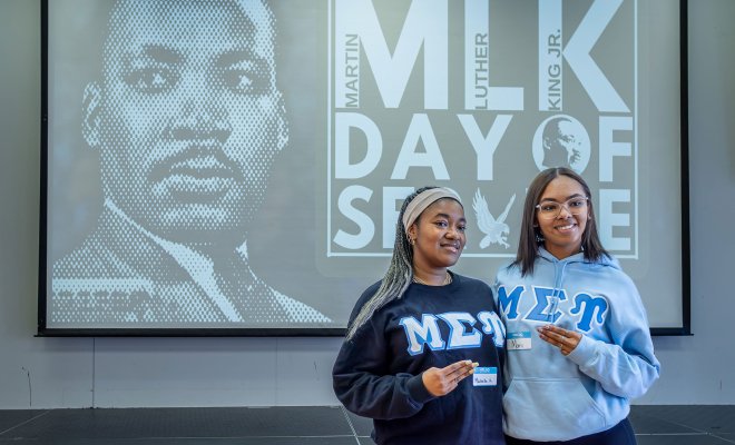 Two sorority members stand before a Martin Luther King Jr.’s Day of Service screen.