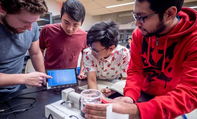 Four students at a lab bench holding a sample and reviewing the readings from an optical scanning device.
