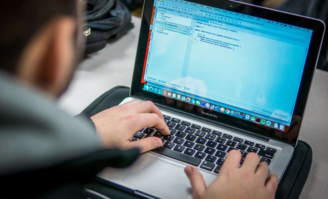 Over-the-shoulder view of a student using a laptop to write an Android app in Java.