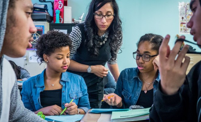 A teacher in a classroom works with a group of middle-school students.