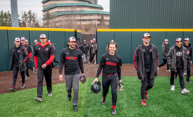 Men in black-and-red Montclair baseball uniforms walk onto a field.