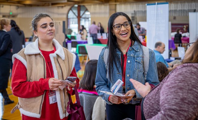 Two students smile and listen to someone speaking.